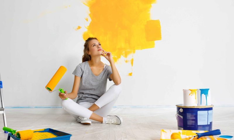 repair in the apartment. Happy young woman paints the wall with  yellow  paint